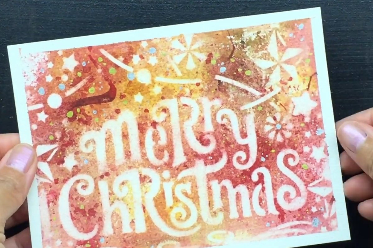 Finished red and orange watercolor card with white Merry Christmas lettering made by reverse stenciling