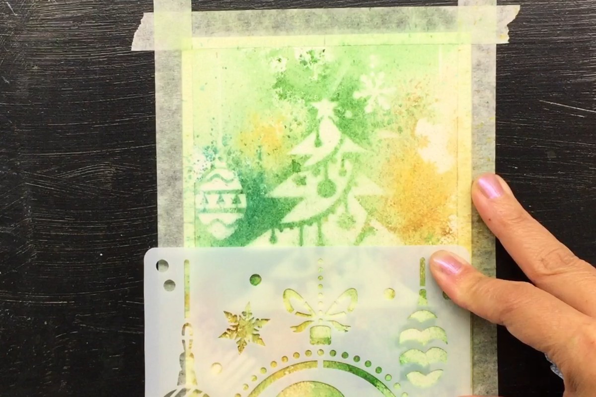 Lifting watercolor through a Christmas ornament stencil on a green and gold tree card